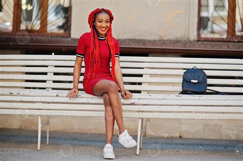 cute and slim african american girl in red dress with dreadlocks and backpack posed outdoor on