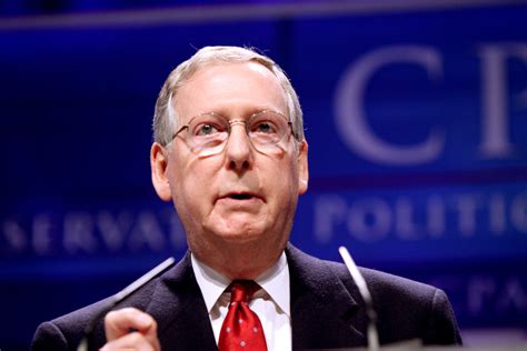 A tightly cropped photograph of discolored, purplish hands bearing a few small bandages, limply hanging from the sleeves of a black suit. Mitch McConnell - Store norske leksikon