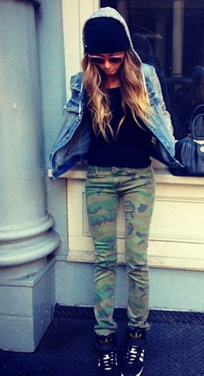 A Woman Standing In Front Of A Window Wearing Camo Pants And A Denim Jacket
