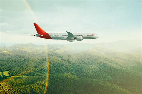 Side View Of A Commercial Airplane Flying Over Green Mountains At