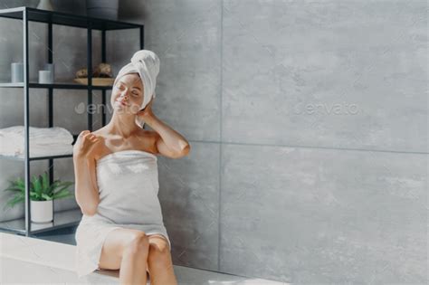 Relaxed Caucasian Female Model Wears Towel Wrapped On Head Feels Refreshed After Taking Shower