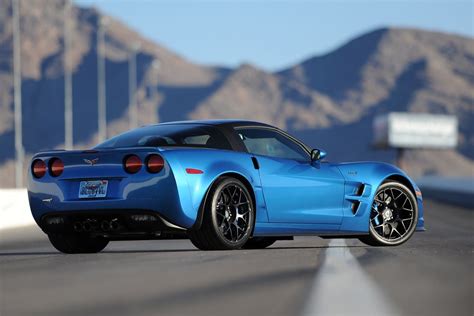 A Blue Sports Car Is Driving Down The Road With Mountains In The Backgroud