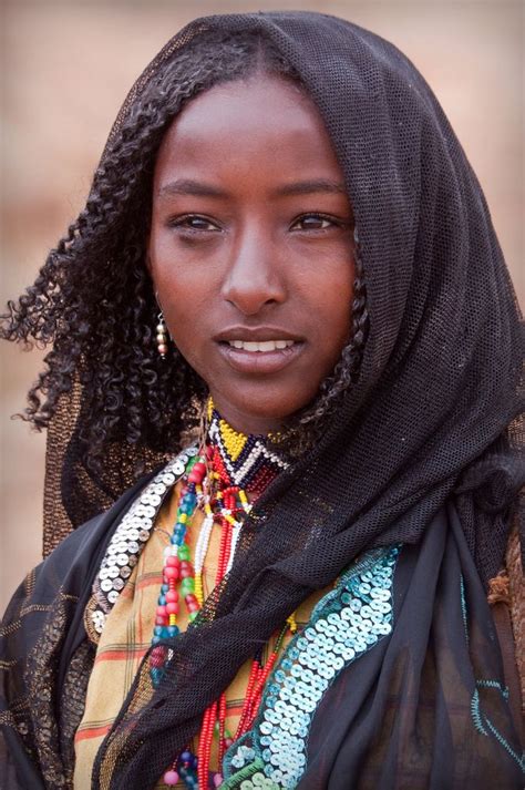 A Woman With Braids Wearing A Scarf And Headdress Is Looking At The Camera