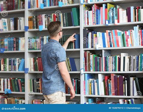 Young Man Taking Book From Shelving Unit In Library Stock Photo Image