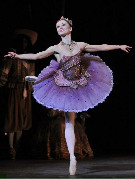 The Ballerina Is Wearing A Purple Tutu And Holding Her Arms Out With