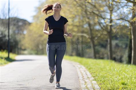 Adult Smiling Fitness Woman Jogging On The Track In The Park Stock