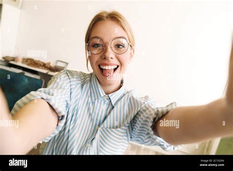 photo of joyful blonde woman in eyeglasses sticking out her tongue while taking selfie photo at