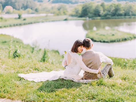 Hugging Newlywed Couple Is Sitting On The Grass And Enjoying Nature