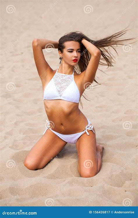 Model In White Bikini Posing Sitting On The Sand At The Beach Stock