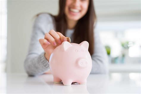 Young Woman Smiling Putting A Coin Inside Piggy Bank As Savings For