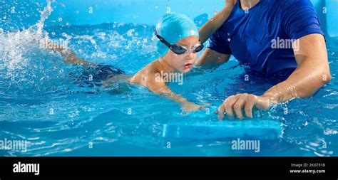Male Trainer Teaching Preschool Boy How To Swim In Indoor Pool With