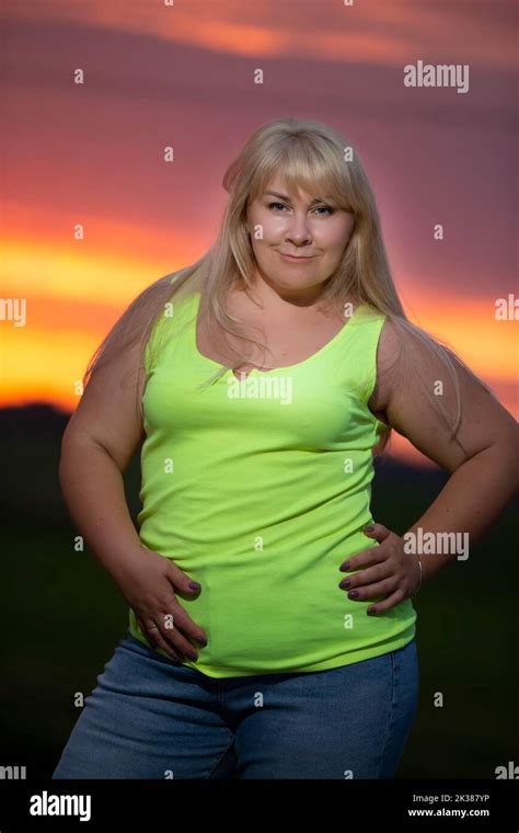 A Plump Middle Aged Woman Poses In Jeans And A Bright T Shirt Against The Background Of The