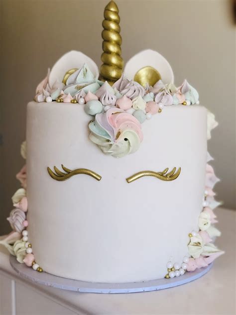A White Cake Decorated With Flowers And A Gold Unicorn Horn On Top Of