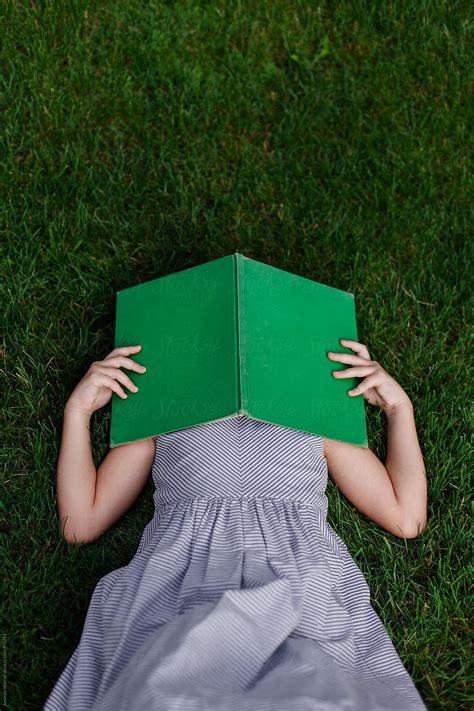 vertical shot of girl laying in grass with vintage book covering her face by stocksy