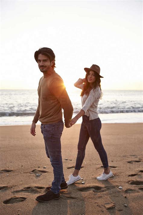 Young Couple Holding Hands While Walking On Beach Stock Photo