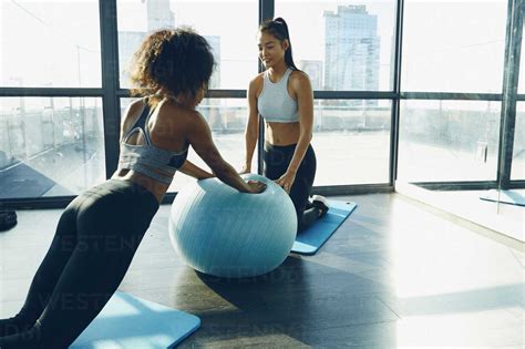 Two Young Women Exercising In Gym Using Inflatable Exercise Ball Stock