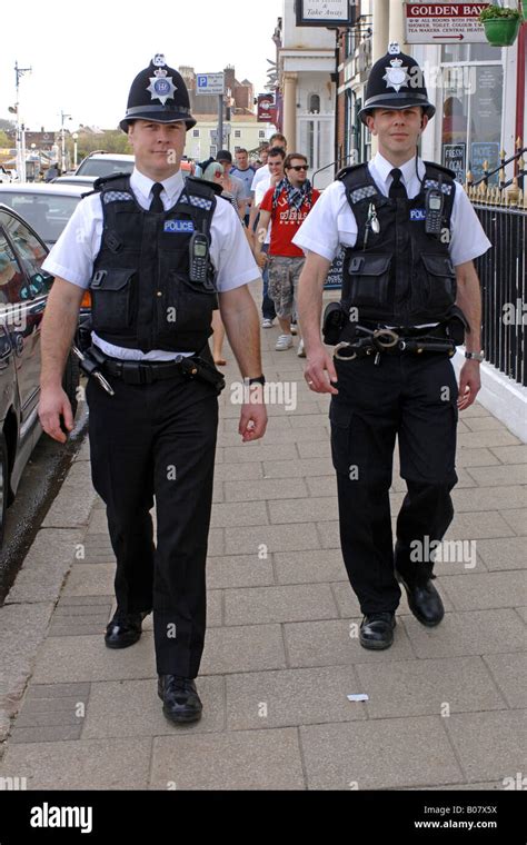 Two British Police Officers Patrolling The Streets Of England Wearing