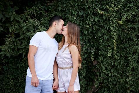 Young Couple In Love Hugging Kissing Near Green Bushes Trees Wall Pretty Blond Woman Wearing