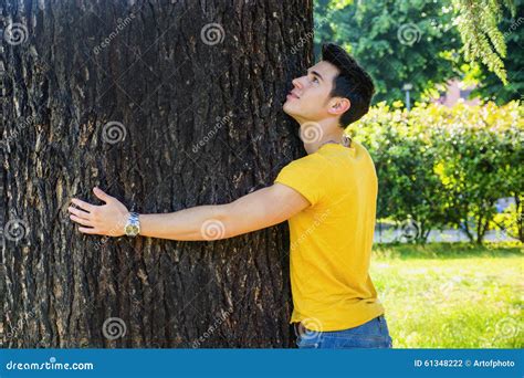Homem Novo De Sorriso Que Abraça Uma árvore Olhando Acima Foto De