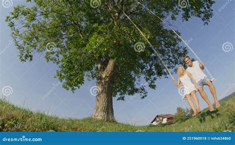 Low Angle Lovely Young Couple Swaying On Swing In Green Meadow In
