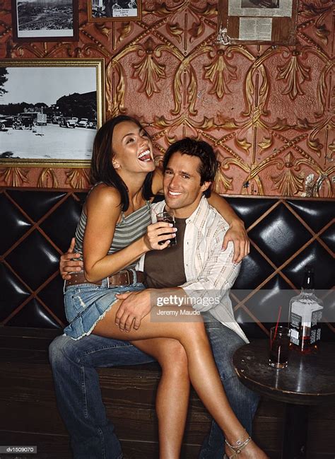Woman Smiling And Drinking Whisky And Sitting On A Mans Lap In A Bar