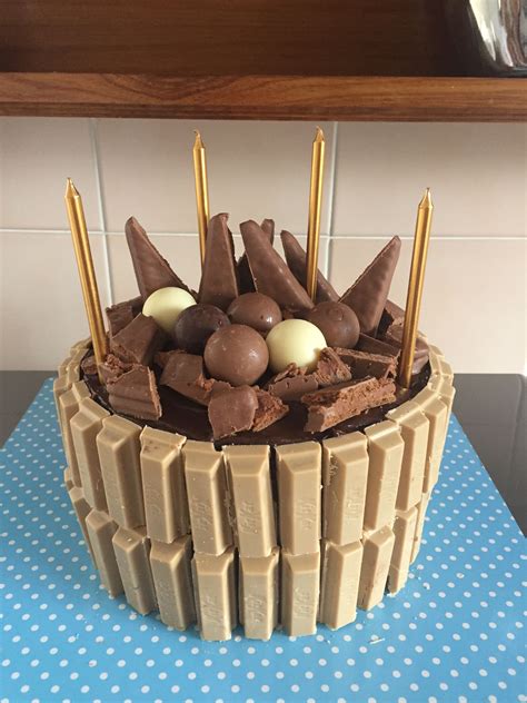 There Is A Cake That Has Chocolate And Candy On The Top With Gold Sticks Sticking Out Of It