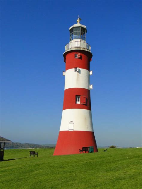 A Red And White Light House Sitting On Top Of A Lush Green Field Under