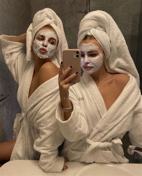 Two Women With Face Masks On Taking A Selfie In Front Of A Bathroom Mirror