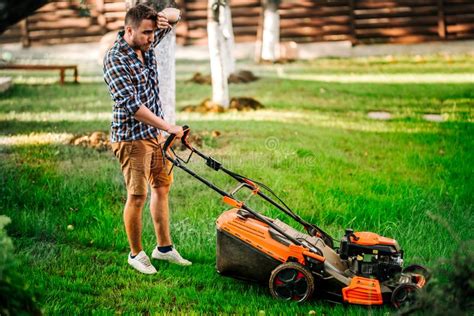 Hard Working Gardener Using Lawnmower And Cutting Grass Stock Photo