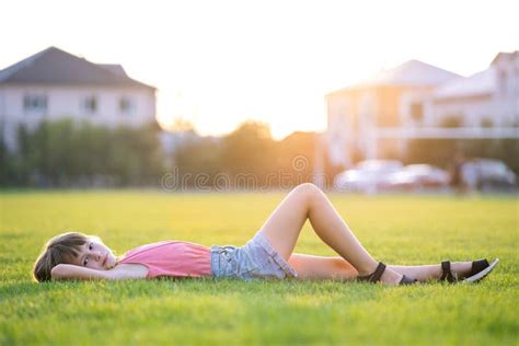 Young Pretty Child Girl Laying Down On Green Grass Lawn On Warm Summer