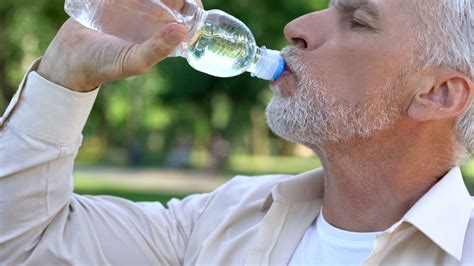 Mature Man Drinking Water From Bottle In Park Maintaining Water