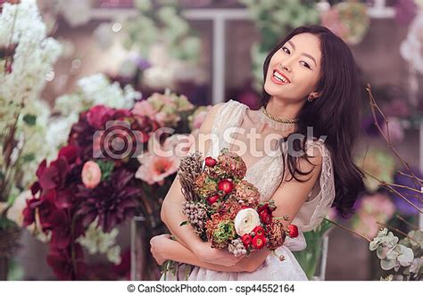 Beautiful Asian Woman Florist In White Dress With Bouquet Of Flowers In Hands In Flower Store