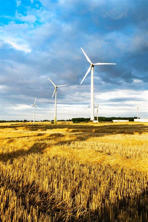 Group Of Wind Turbines In The Golden Field Against A Blue Clouded Sky