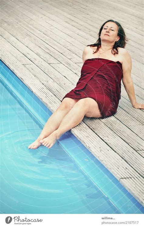 Mature Brunette Woman Sunbathing By The Pool With Her Feet In The Water