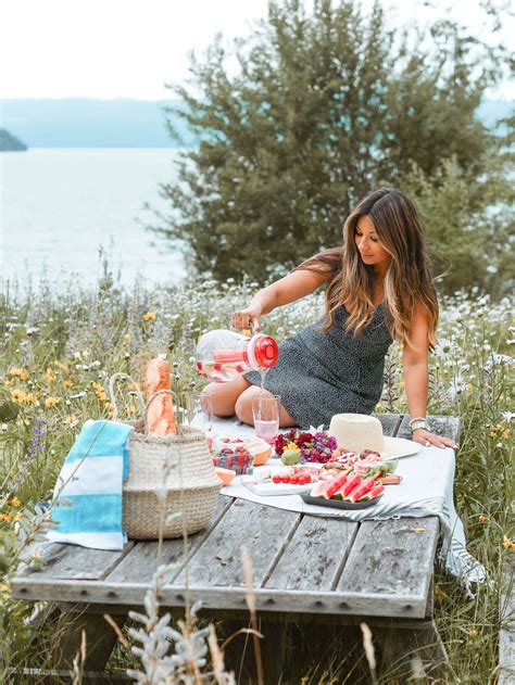 A Woman Sitting At A Picnic Table With Food And Drinks In Front Of Her On The Water