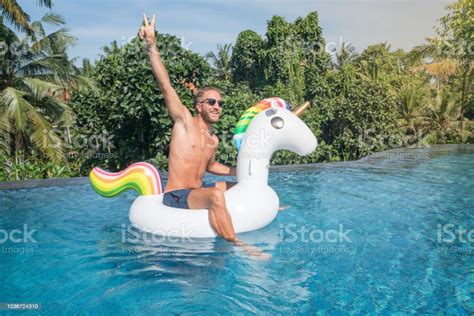 Young Man On Inflatable Unicorn Having Fun In Hotel Swimming Pool