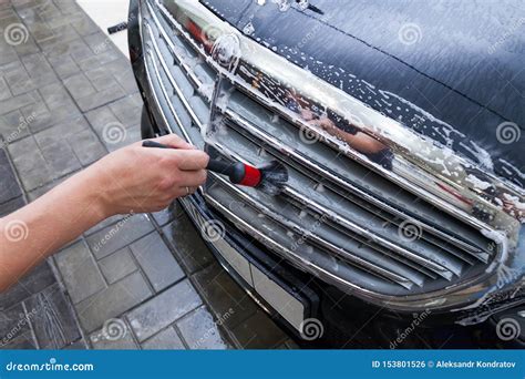 A Male Worker Washes A Black Car With A Special Brush For Grille And Scrubs The Surface To Shine