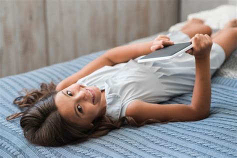jeune fille souriante allongée sur le lit tenant une tablette numérique à la main photo gratuite