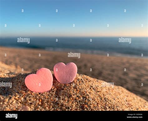 Two Candy Hearts Sitting On A Sandy Beach With Ocean On The Horizon At