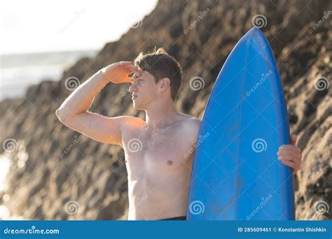 A Man With Naked Torso Looking In The Distance Holding A Surfboard
