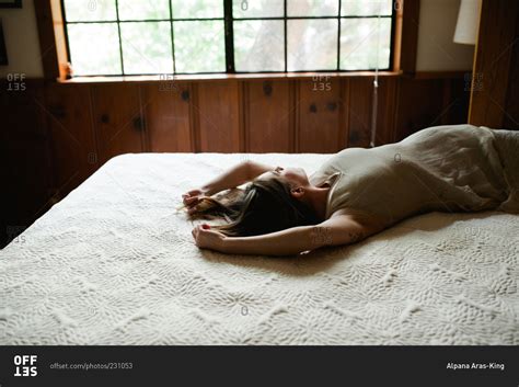 Woman Stretched Out On Bed Gazes Out Window Stock Photo OFFSET