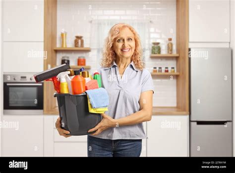Mature Woman Holding A Bucket With Cleaning Supplies Inside A Modern