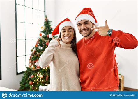 Young Hispanic Couple Standing By Christmas Tree Smiling Cheerful