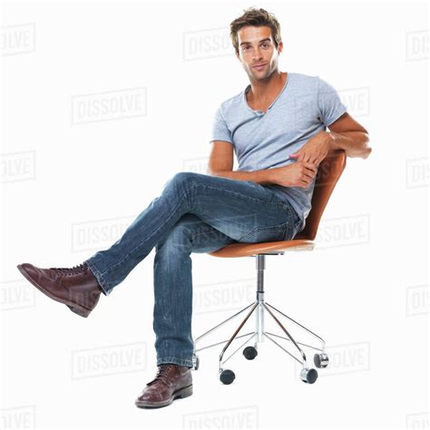 Portrait Of Young Man Sitting On Chair With Legs Crossed Against White