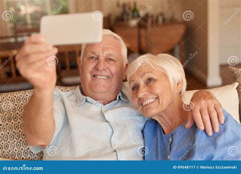 smiling senior couple taking cellphone selfies together on their sofa stock image image of