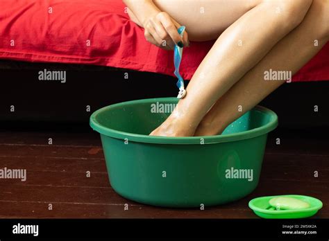 The Girl Shaves Her Legs That Are In A Green Plastic Bowl On The Wooden