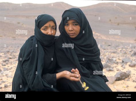 arab girls in black burkhas sitting close together pick a desert flower in remote desert