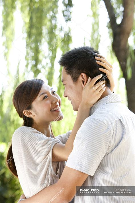 Young Chinese Couple Embracing Under Willow Tree In Park — Looking Up