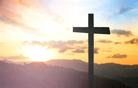 Silhouette Cross On Mountains Against Cloudy Sky During Sunset Stock Photo