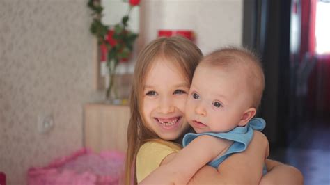 Young Beautiful Girl Holding Her Little Brother In Her Arms Smiling